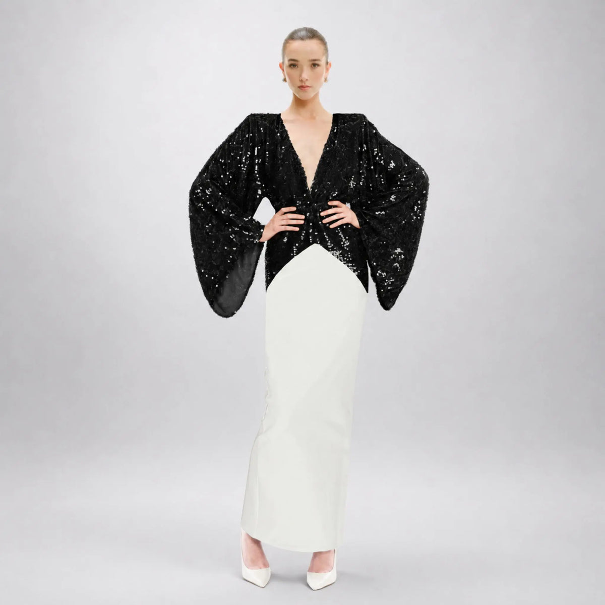 A model wearing a black avaro-figlio sequined long-sleeve top with dramatic bell sleeves and a white pencil skirt, standing against a light gray studio background.