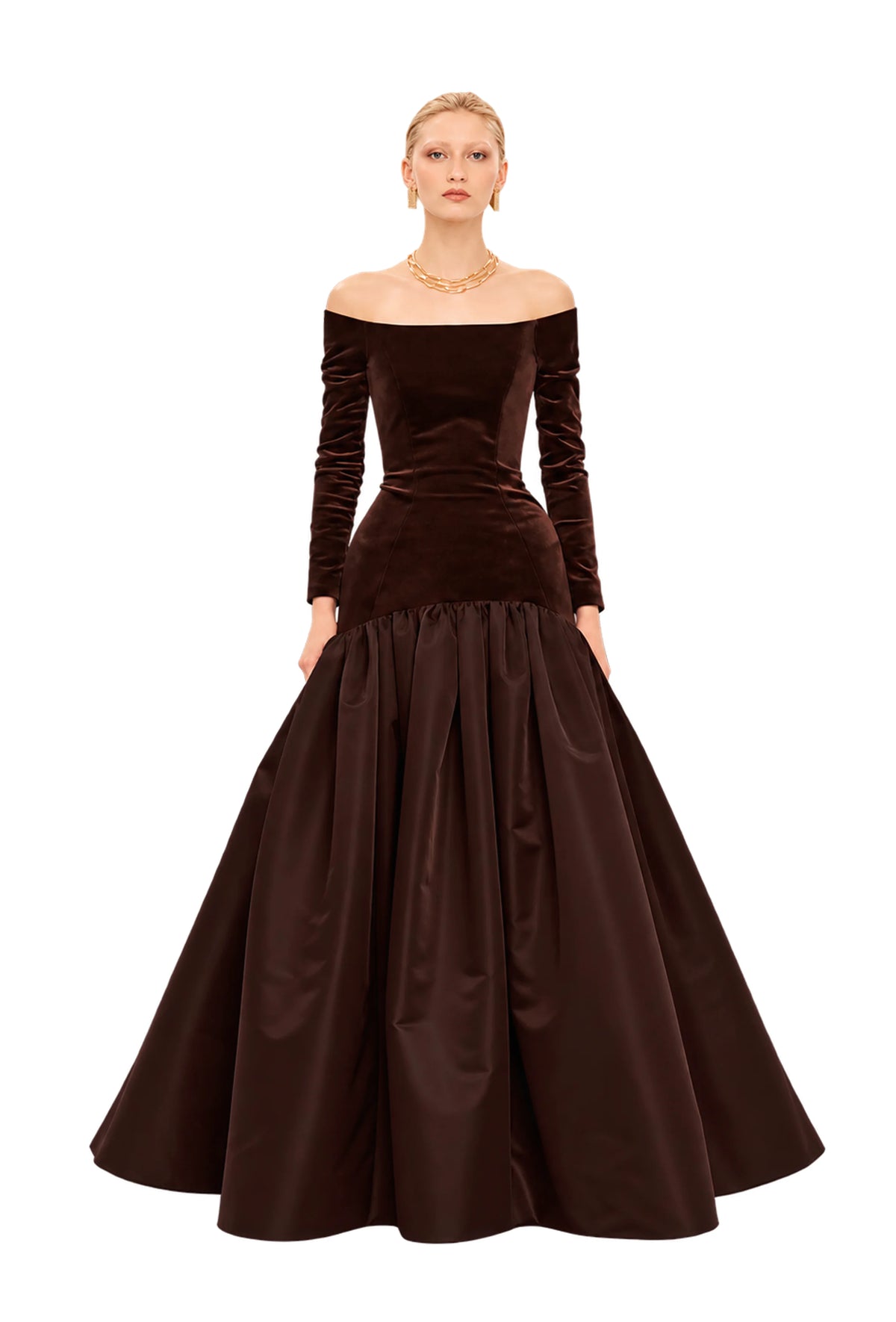 Model wearing an off-the-shoulder Avaro Figlio long-sleeve ball gown in dark brown velvet and satin, photographed against a light gray studio background.