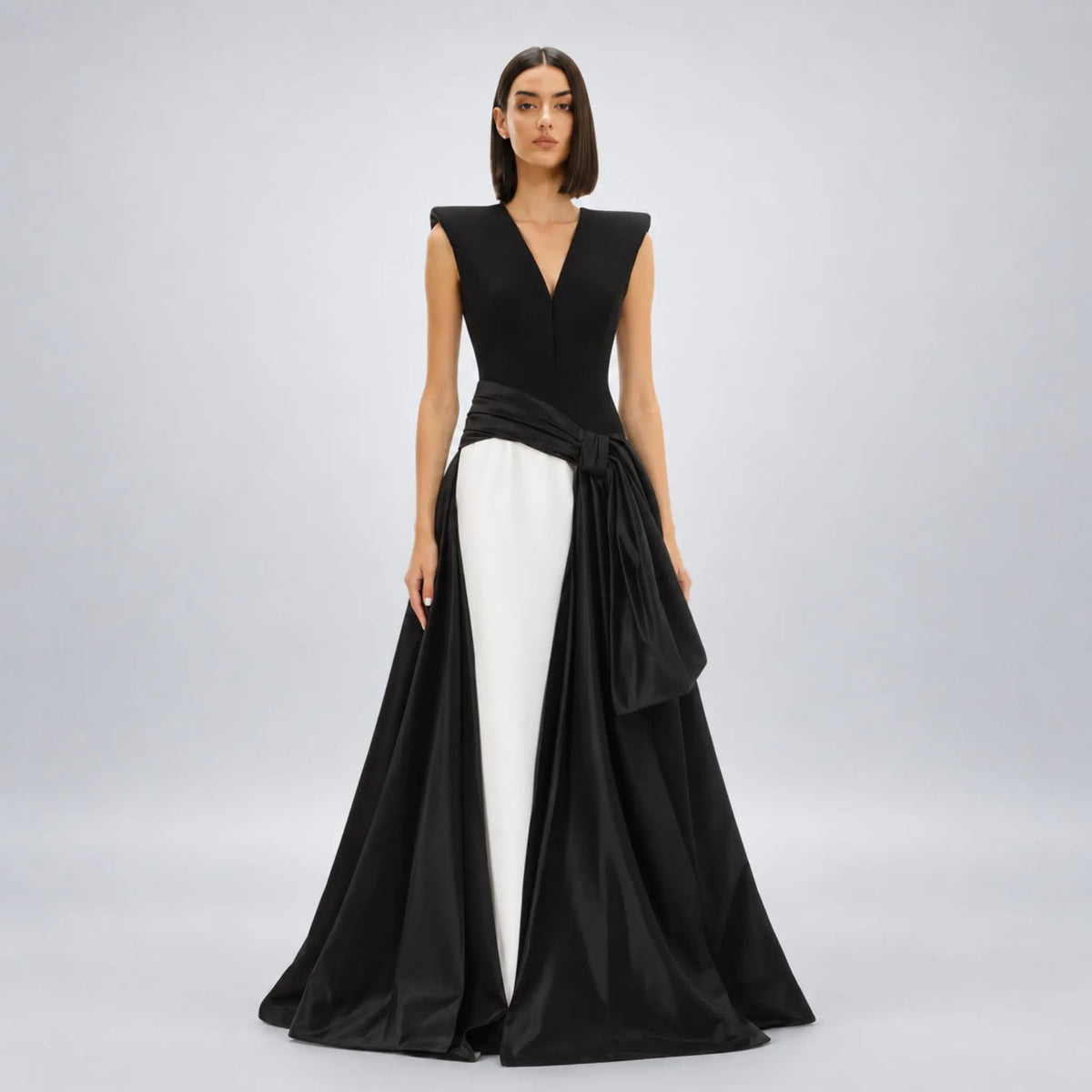 Model wearing a black and white avaro figlio formal gown with a structured black bodice, a wide black waist sash tied in a bow, and a flowing black skirt, displayed on a white mannequin against a white background.