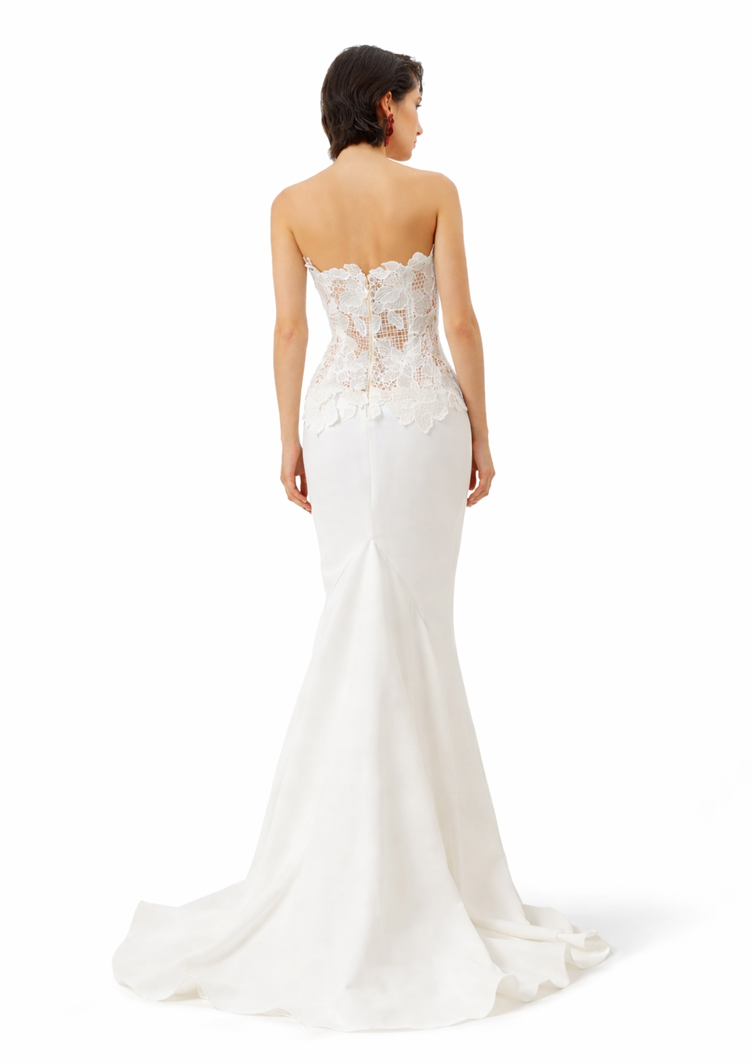 Woman wearing a strapless white wedding dress with lace details on a white background
