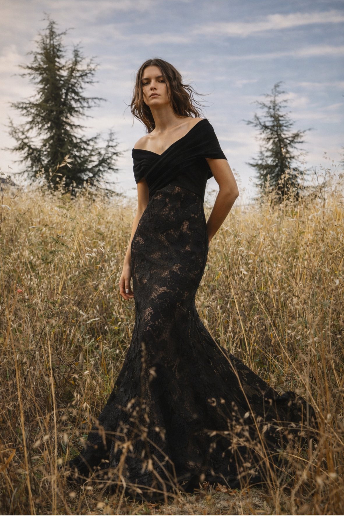 Woman in a black lace dress standing in a field with trees in the background