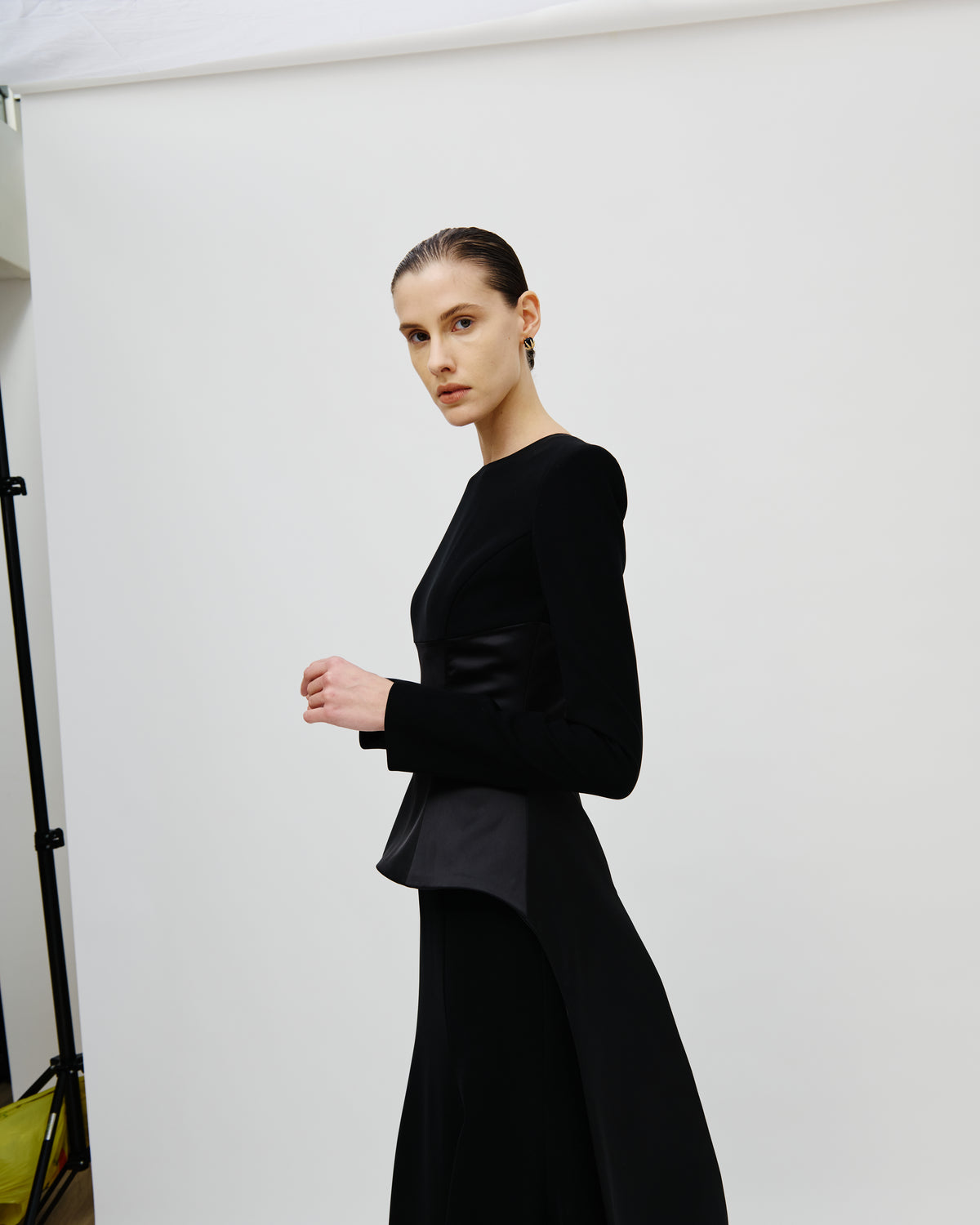 A model wearing an Avaro Figlio black long-sleeve dress with a structured velvet-like bodice and a flared skirt, photographed against a plain white studio backdrop.
