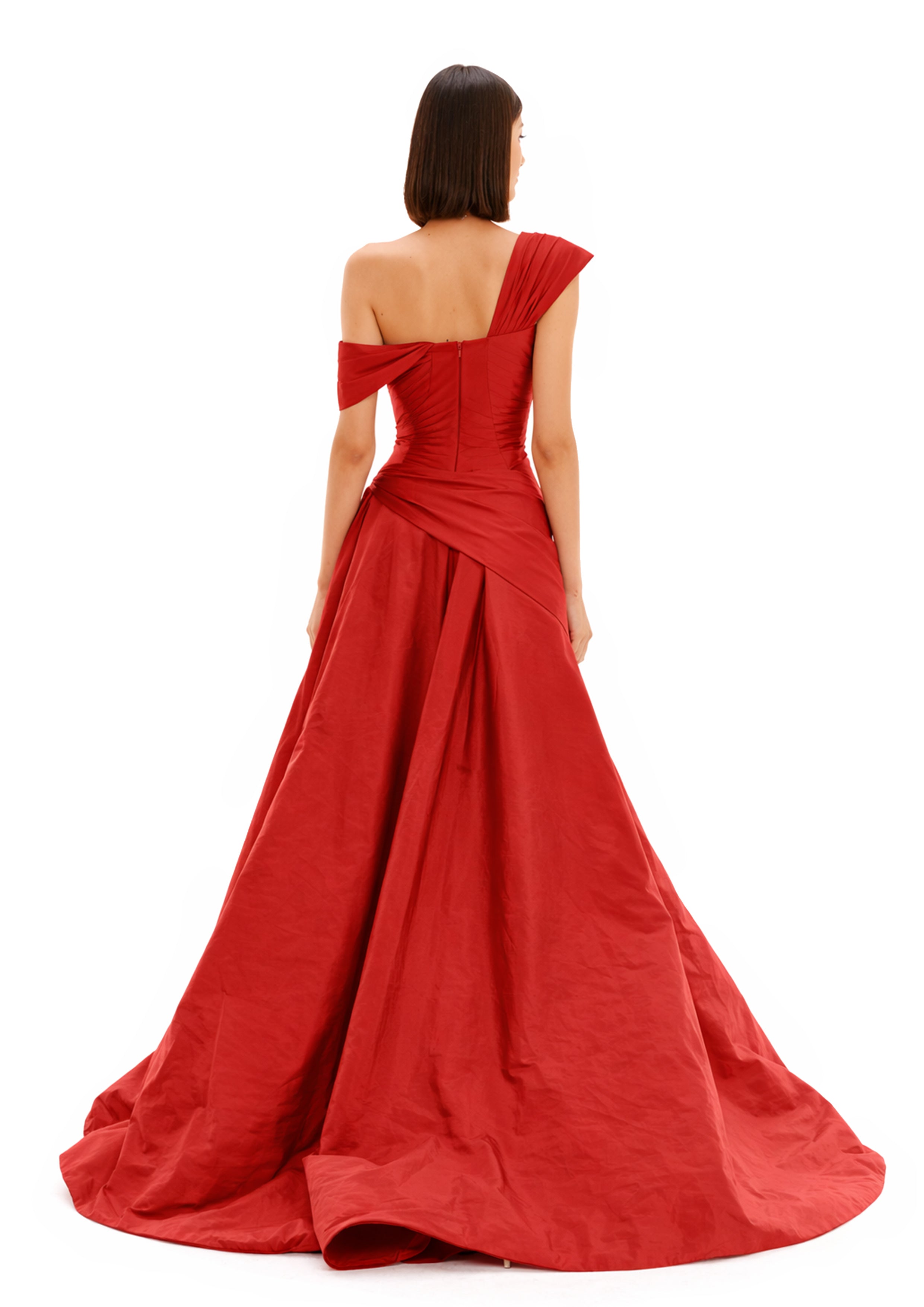 Back view of a model wearing a ONE-SHOULDER DRAPED BALL GOWN in red with a flowing train.