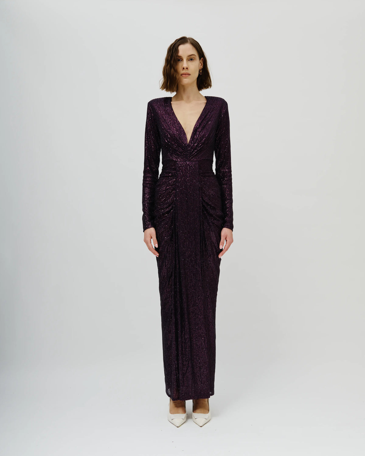 A woman modeling an Avaro Figlio long-sleeved, deep V-neck maxi dress in a textured, deep plum purple fabric, standing against a light gray studio background.