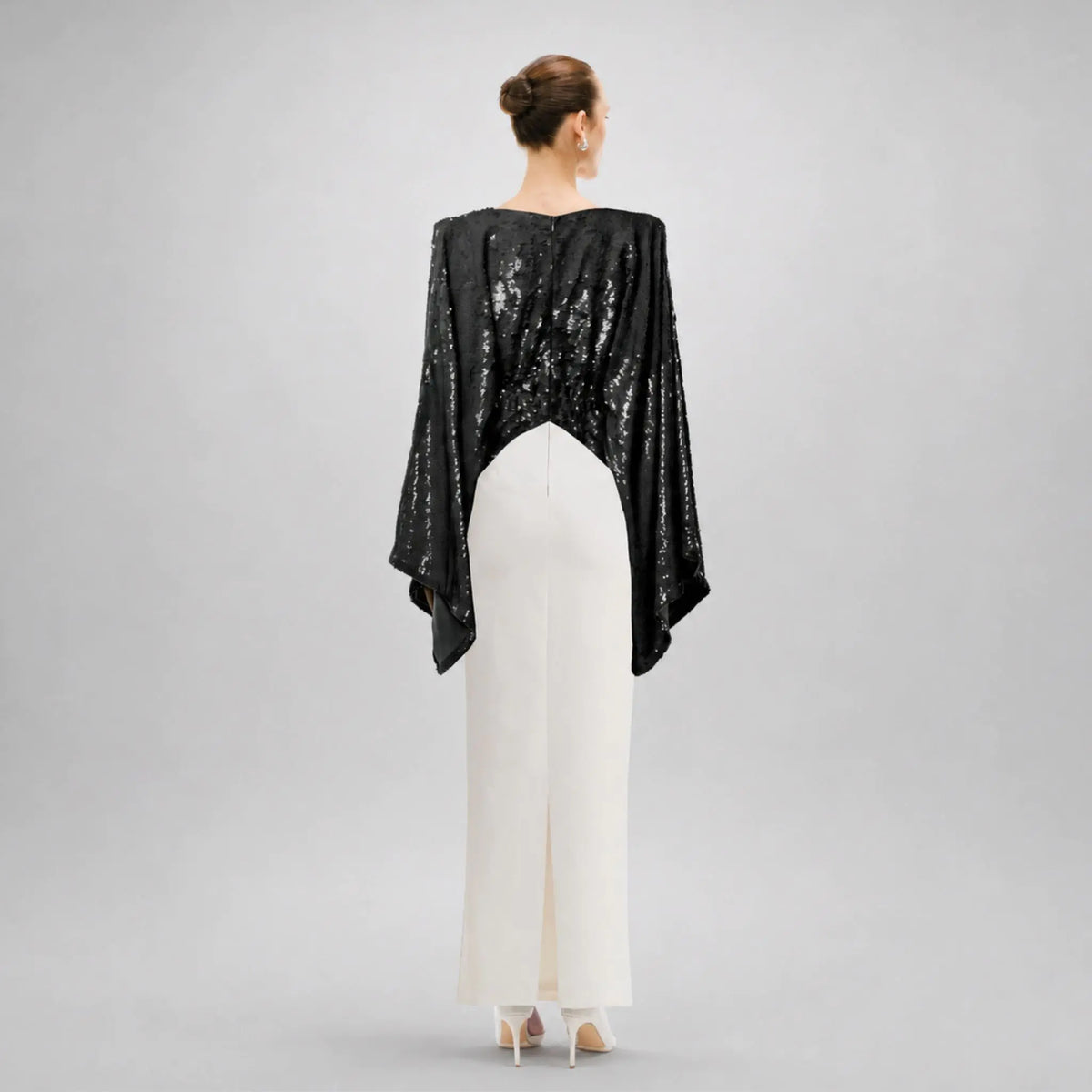 Back view of a model in a black sequin kimono dress with white cady, showcasing elegant eveningwear style.