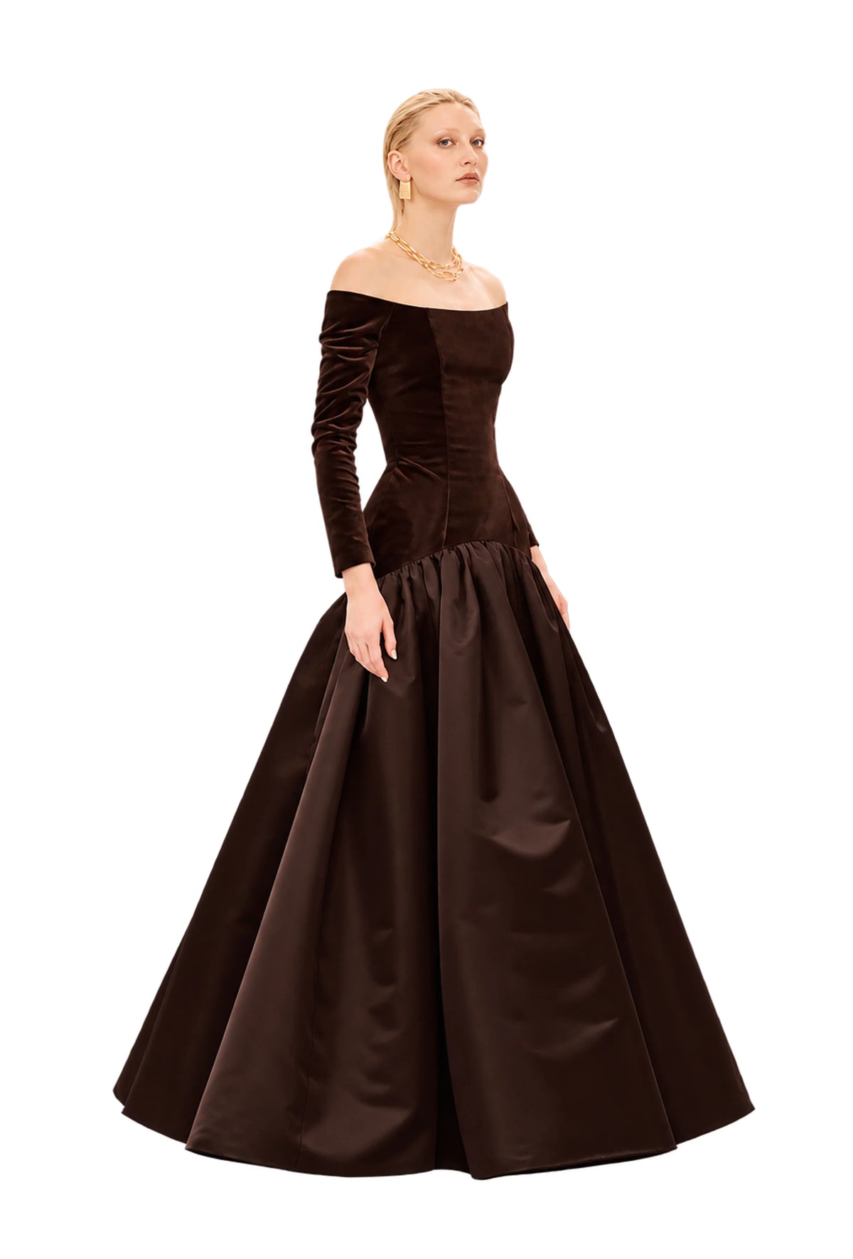A woman modeling an off-the-shoulder Avaro Figlio long-sleeve ball gown in dark brown velvet and satin, photographed against a light gray studio background.