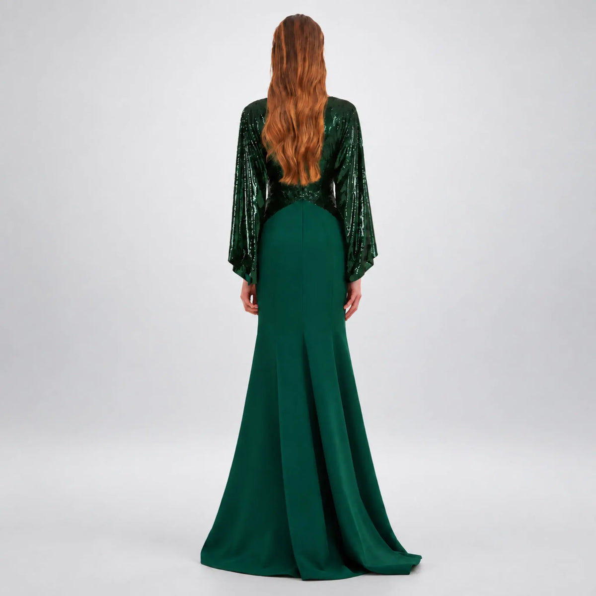 A woman viewed from the back wearing a floor-length avaro figlio forest green kimono maxi dress with long sheer sleeves covered in sequins and a fitted skirt, photographed against a light gray studio background.