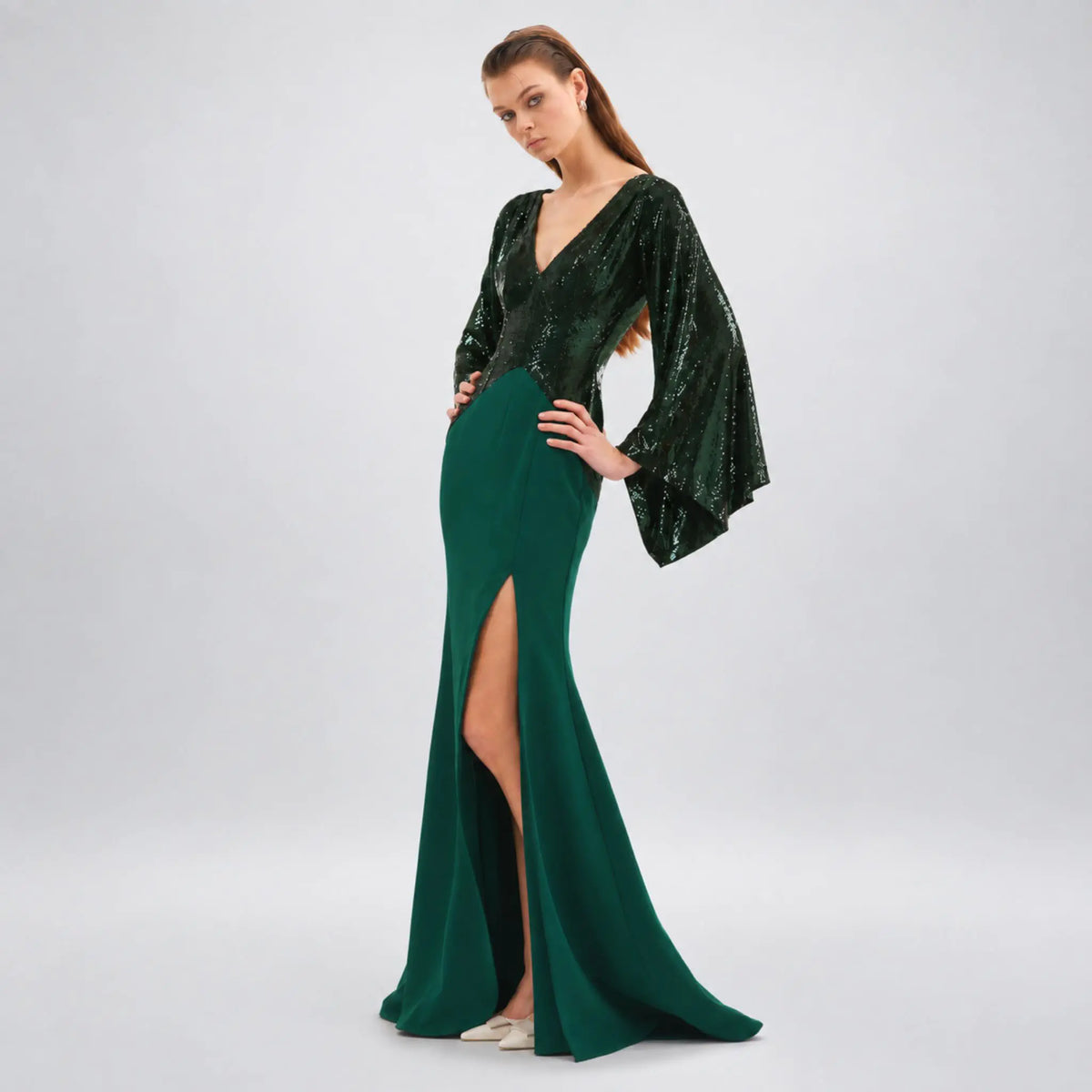 A model wearing a floor-length avarofiglio forest green evening kimono maxi dress with a sequined bodice, wide bell sleeves, and a thigh-high slit, photographed against a light gray studio background.
