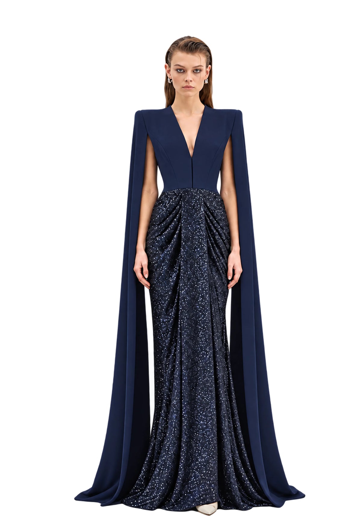 A model stands against a light gray studio background wearing a floor-length Avaro Figlio gown with a deep V-neckline, structured cap sleeves, and a long flowing cape. The bodice is a solid dark navy, while the skirt is a shimmering dark blue-gray textured fabric with a draped, gathered silhouette.