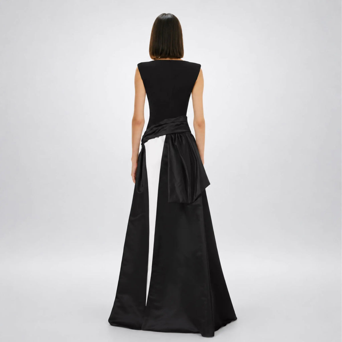 Model wearing a black and white avaro figlio formal gown with a structured black bodice, a wide black waist sash tied in a bow, and a flowing black skirt, displayed on a white mannequin against a white background.