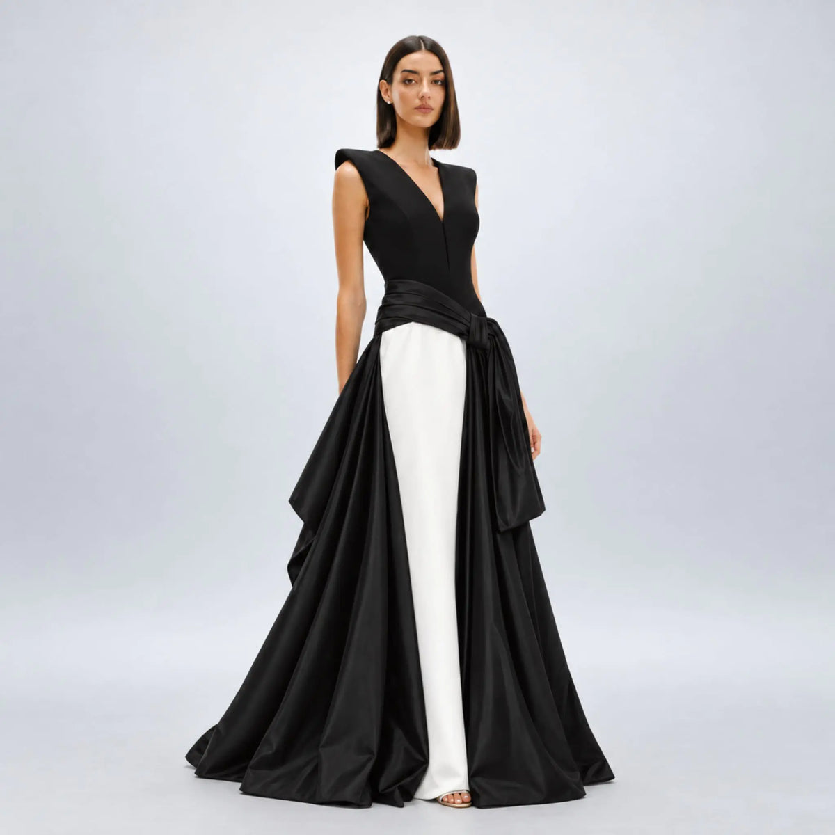Model wearing a black and white avaro figlio formal gown with a structured black bodice, a wide black waist sash tied in a bow, and a flowing black skirt, displayed on a white mannequin against a white background.