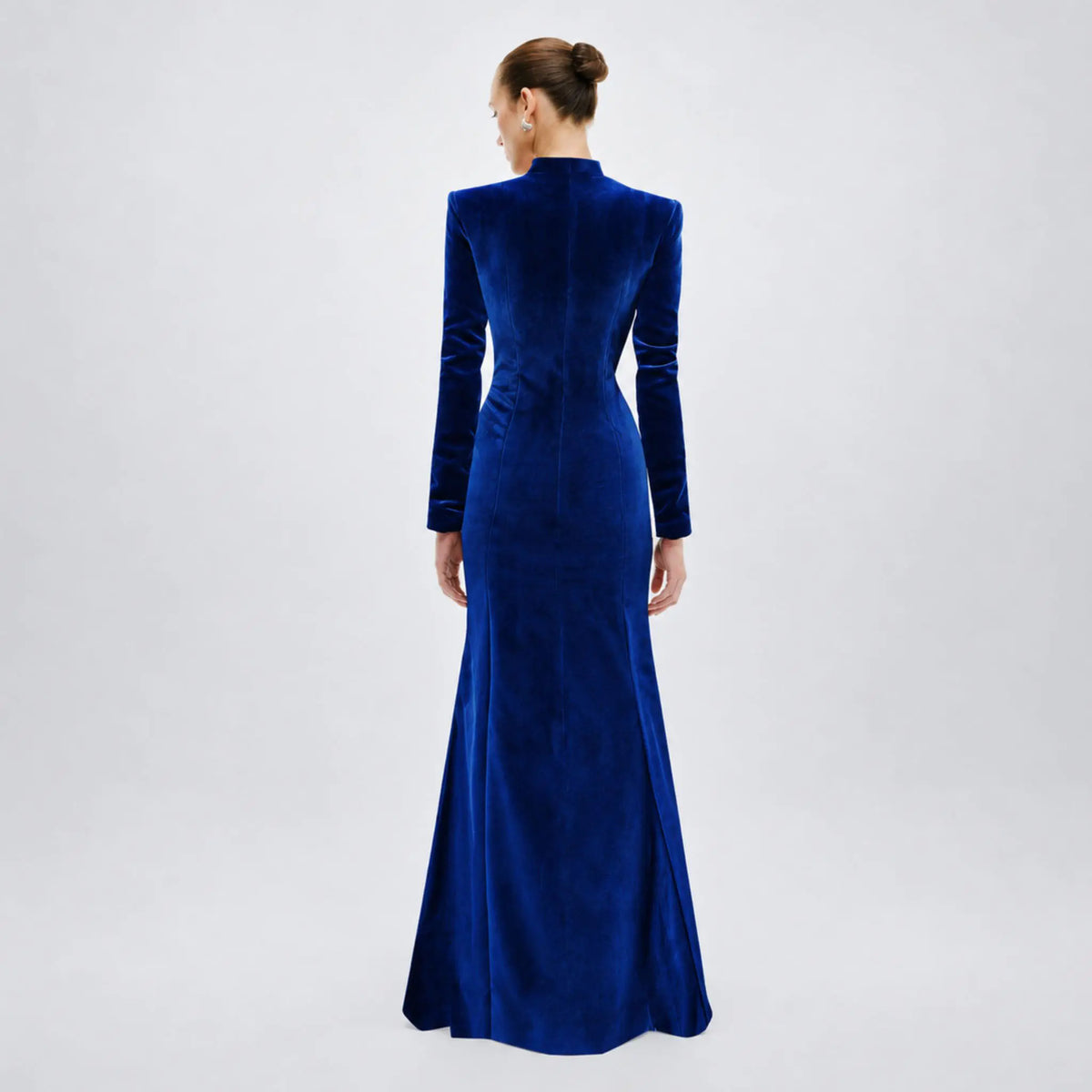 A woman viewed from the back wearing a long-sleeved avaro figlio royal blue velvet floor-length gown against a light gray studio background.