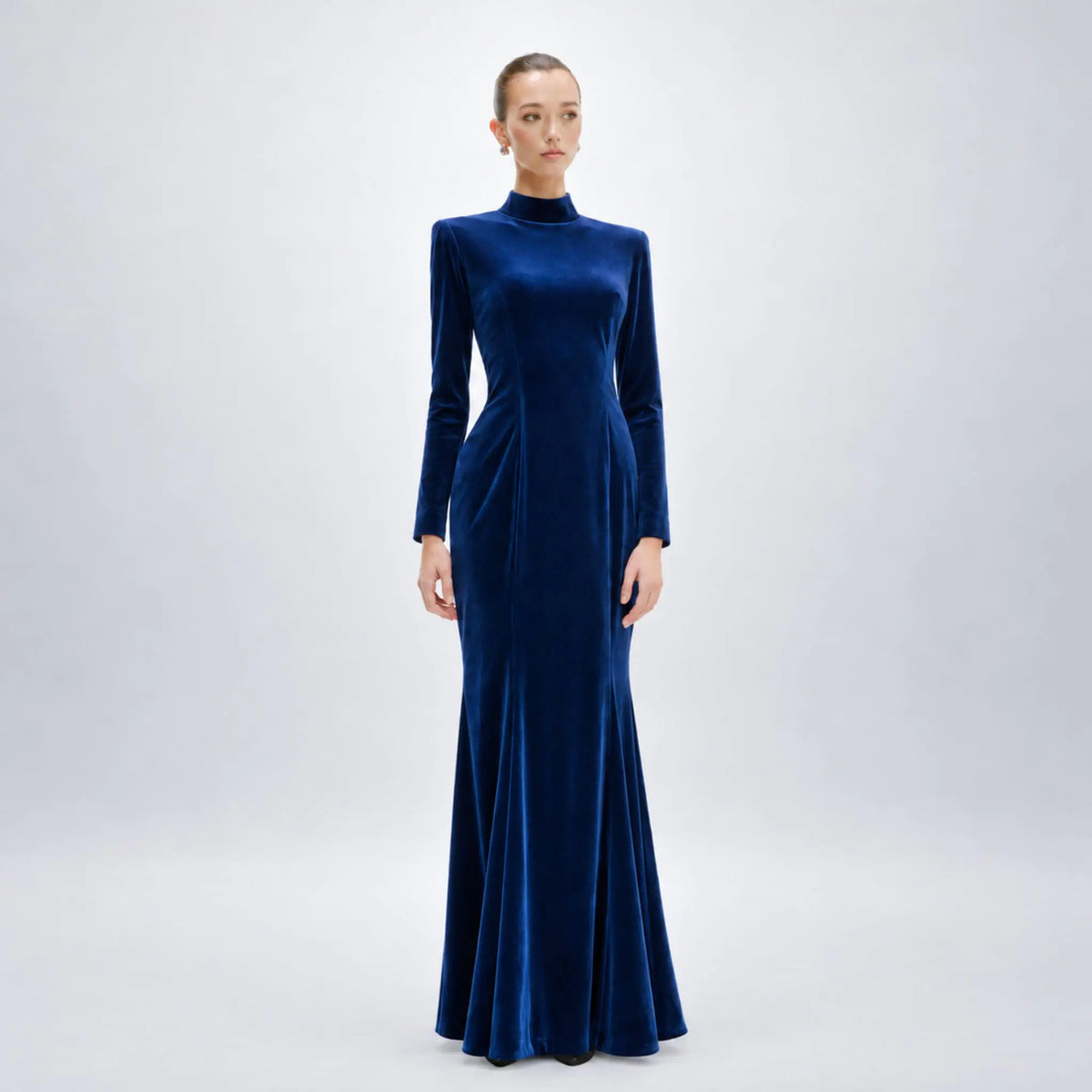 Model wearing Avaro Figlio long-sleeved, high-neck floor-length avaro figlio gown in rich royal blue velvet against a light gray studio background.